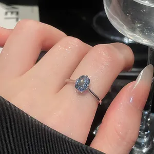 Detailed view of an elegant silver open ring with a sparkling blue gemstone on a finger.