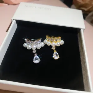 Detailed close-up of gold and silver ear cuffs with pearls and teardrop zircon.