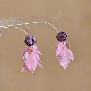 Close-up view of the sweet fabric rose and pink acrylic petal tassel earrings on a stand.