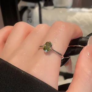 Close-up of a vintage silver ring with a square olive green gemstone worn on a finger.