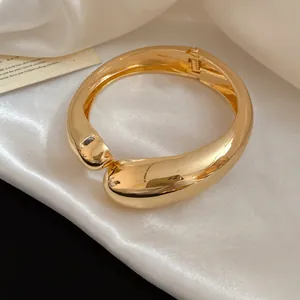 Close-up of a thick gold-toned irregular metallic chunky bangle on elegant white silk