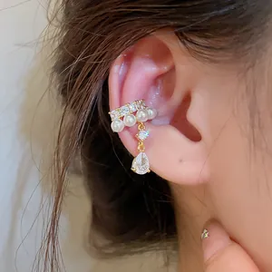 Macro view of an elegant gold-toned ear cuff featuring white pearls and a sparkling teardrop zircon dangle