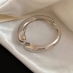 Close-up detail of a silver-toned asymmetrical wrinkled metallic bangle on silk fabric