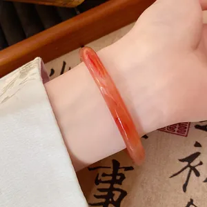 Close-up of a red translucent glass bangle worn on wrist with traditional Hanfu sleeve.