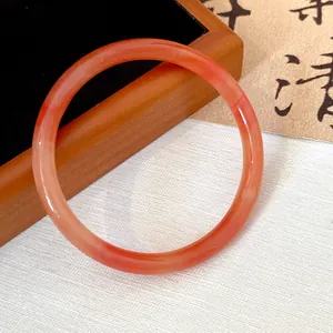 Close-up of a translucent red glass bangle on a wooden stand with oriental calligraphy background