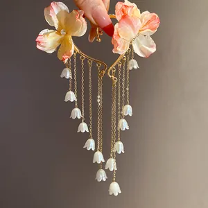Dettaglio macro di fiori in tessuto e nappe di perle mughetto su polsini da orecchio