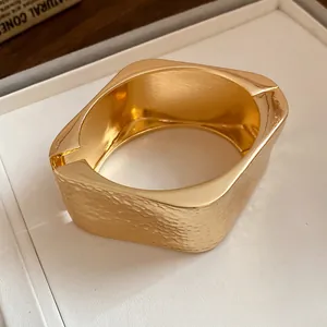 Close-up detail of a golden metal bracelet featuring a textured wrinkled hammered finish