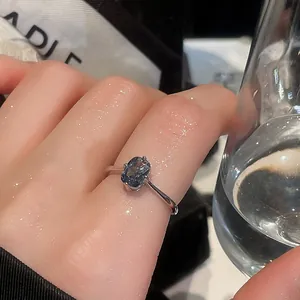 Macro view of minimalist silver ring with sparkling oval blue gemstone on finger