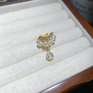 Detailed macro view of an elegant gold ear cuff with pearls and a teardrop zircon dangle