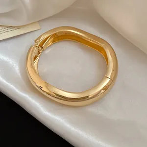 Macro view of a luxurious gold-tone wavy chunky metal bangle on white silk fabric