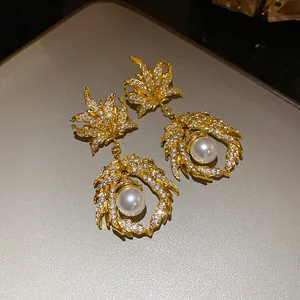 Detailed macro view of vintage gold earrings featuring zircon maple leaf and elegant pearl pendant