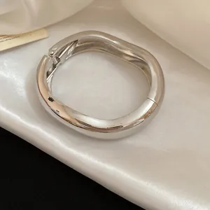 Detail macro view of polished silver metal wavy wrinkled bracelet on white satin fabric