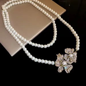 Close-up of an elegant long pearl necklace featuring two sparkling rhinestone flower pendants