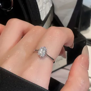Close-up of a minimalist silver-toned ring featuring a clear oval faceted gemstone on a hand.