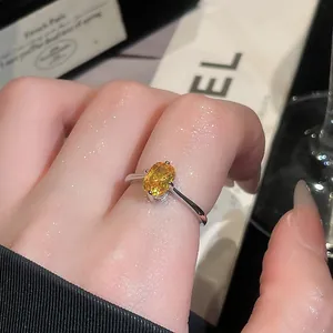 Close-up detail of a silver-toned ring featuring a vibrant yellow oval gemstone on a finger.