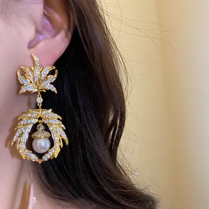 Macro detail view of a vintage gold maple leaf drop earring with zircon and pearl decor.