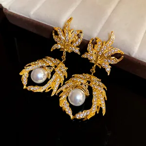 Detailed close-up of golden maple leaf earrings featuring white pearls and zircons
