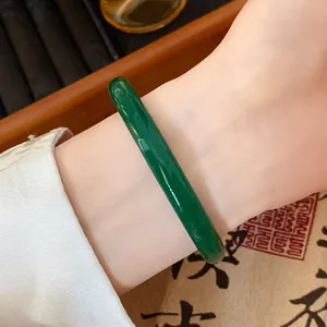 Close-up of a deep green jade-like glass bangle worn on a wrist in traditional style