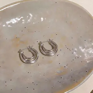 Elegant minimalist silver-tone triple hoop earrings displayed on a rustic ceramic dish.