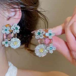 Close-up of sparkling flower earrings with pavé zircons and colorful oval stones.