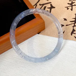 Close-up of a translucent bluish glass bangle on white cloth with calligraphy