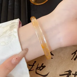 Close-up detail of a transparent amber glass bangle worn on a wrist with Hanfu sleeve