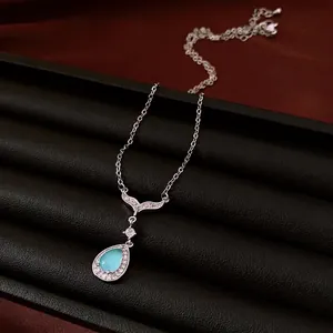 Collier élégant en argent avec pendentif goutte en zircon bleu sur présentoir noir.