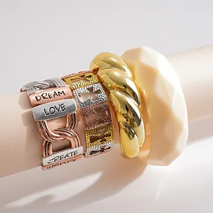 Detailaufnahme von gravierten Metallarmbändern und einem cremefarbenen Acrylarmreif