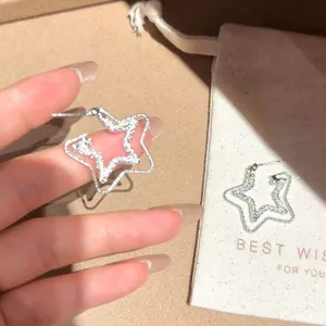 Dettaglio ravvicinato di orecchini a stella in argento lucido con sacchetto regalo.
