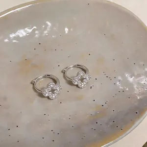 Detailed macro view of elegant silver zircon clover earrings on a ceramic tray