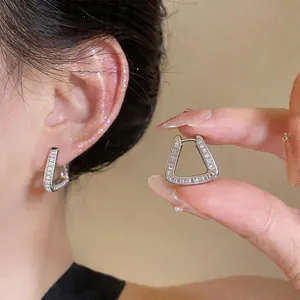 Close-up of elegant silver trapezoidal hoop earrings with zirconia on a model's ear.