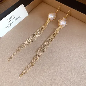 Macro view of elegant gold long tassel earrings with pearl in delicate wire cage