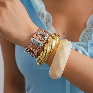 Detailansicht von geschichteten Metallarmbändern und einem cremefarbenen Acrylreif