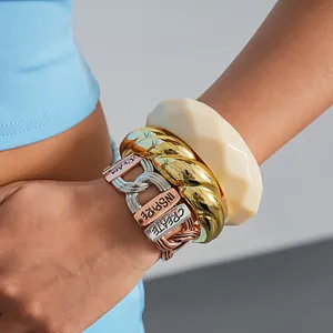 Nahaufnahme von klobigem Acryl-Armreif und dreifarbigem Metallarmband mit Gravuren