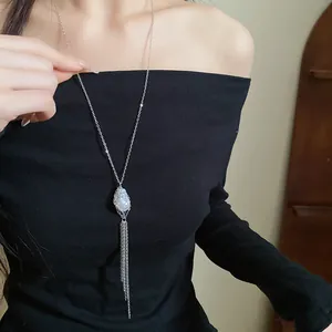 Elegant long silver tassel necklace with pearl pendant worn on black dress model.