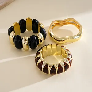 Detail view of chunky gold and tortoiseshell acrylic geometric bracelets on beige surface