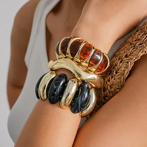 Close-up detail of chunky acrylic and gold geometric statement bracelets on a model's arm