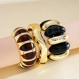 Close-up of chunky gold-tone and contrast acrylic geometric bracelets on pink stand