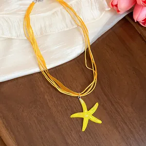 Close-up detail of yellow resin starfish pendant with multiple orange silk ribbons necklace