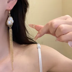 Detail shot of elegant long golden tassel earrings with a pearl accent on a model