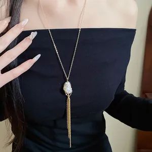 Detail view of a long gold tassel necklace featuring a unique mesh-wrapped baroque pearl pendant