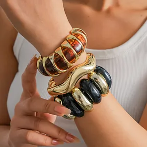 Close-up of stacked chunky geometric acrylic bracelets in amber, black, and gold.
