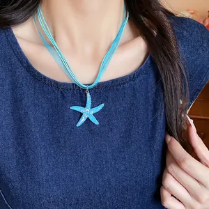 Detail of vacation style light blue resin starfish necklace worn on a female model