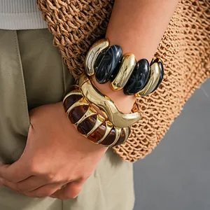 Close-up of chunky marble swirl and amber acrylic bangles with gold metal details