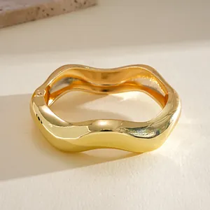 Close-up view of a gold-tone wavy geometric bangle with a glossy finish and hinge detail