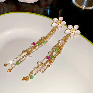 Close-up of elegant gold tassel earrings with white enamel flowers and colorful beads