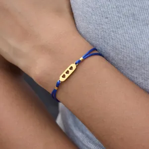 Dettaglio ravvicinato di un braccialetto blu intrecciato con triplo cuore dorato.