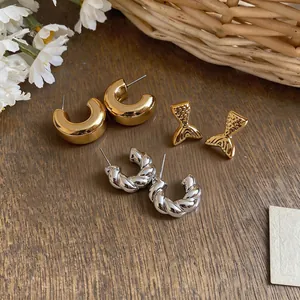 Detail view of stylish gold and silver C-shape hoops and fishtail stud earrings on wood