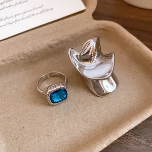 Anello intrecciato argento con gemma blu e dettaglio accessorio a cappello abbinato.