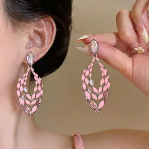 Macro close-up view of pink enamel drop earrings with rhinestone accents on a model